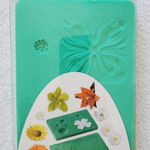May include: A Wilton Flower Impression Set in a clear plastic package. The set includes two green rectangular silicone impression mats for gum paste. The packaging displays the text Flower Impression Set and dimensions of 4.5 x 6.5 inches and 4.5 x 7.5 inches.