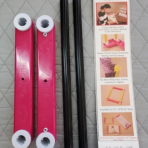 May include: A needlework ratchet frame kit with pink supports, black rods, and a product information card. The pink supports have white ends and a rose design. The card displays product features and the brand name.