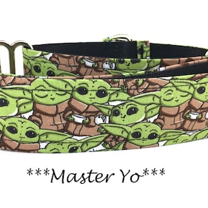 May include: A black and white dog collar with a repeating pattern of green cartoon characters holding cups. The collar has silver hardware and the text "***Master Yo***" is printed below the collar.