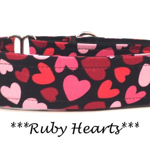 May include: A black dog collar with a red and pink heart pattern. The collar is made of fabric and has silver hardware. The text "***Ruby Hearts***" is printed below the collar.