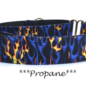 May include: A dog collar with a blue flame pattern, featuring yellow and orange flames against a dark blue background. The collar has metal hardware and the word "Propane" is written in cursive.