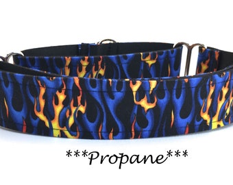 May include: A dog collar with a blue flame pattern, featuring yellow and orange flames against a dark blue background. The collar has metal hardware and the word "Propane" is written in cursive.