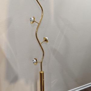 May include: A gold-colored, vintage floor lamp with a curved stem and four light fixtures. The lamp has a round base and a sleek, modern design. The cord is black.