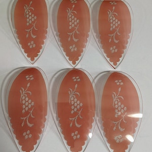 May include: Six clear glass serving dishes with a peach-colored center and a white grape design. The dishes have a teardrop shape with a scalloped edge, perfect for serving appetizers or desserts.