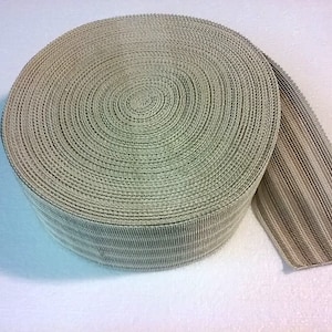 May include: A roll of beige elastic trim with a ribbed texture. The trim is rolled up and a portion is unrolled, showing the ribbed texture.