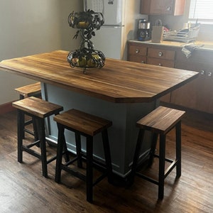 Peut inclure: Un &icirc;lot de cuisine en bois clair avec une base grise et quatre tabourets de bar en m&eacute;tal noir. L'&icirc;lot a un comptoir en bois et un bol &agrave; fruits en m&eacute;tal d&eacute;coratif.