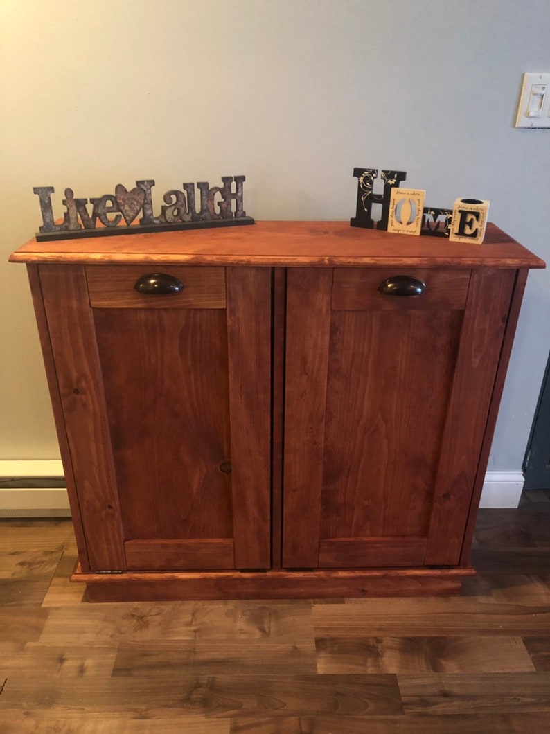 K&ouml;nnte beinhalten: Ein Holzschr&auml;nkchen mit zwei T&uuml;ren und zwei Schubladen. Der Schrank ist in einem dunklen Braunton gebeizt und hat schwarze Metallgriffe. Der Schrank ist mit den Worten "Live Laugh" und "Home" verziert.