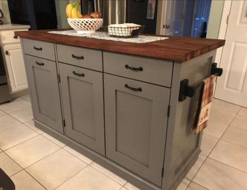 Puede incluir: Una isla de cocina gris con una encimera de madera y cuatro puertas de armario. La isla tiene herrajes negros y un toallero en el lateral.