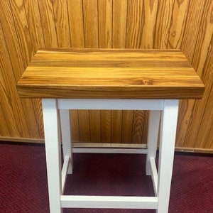 Peut inclure: Un tabouret en bois blanc avec un plateau en bois de boucher. Le plateau est en bois avec une finition naturelle. Le tabouret a un design simple avec quatre pieds et une barre transversale.