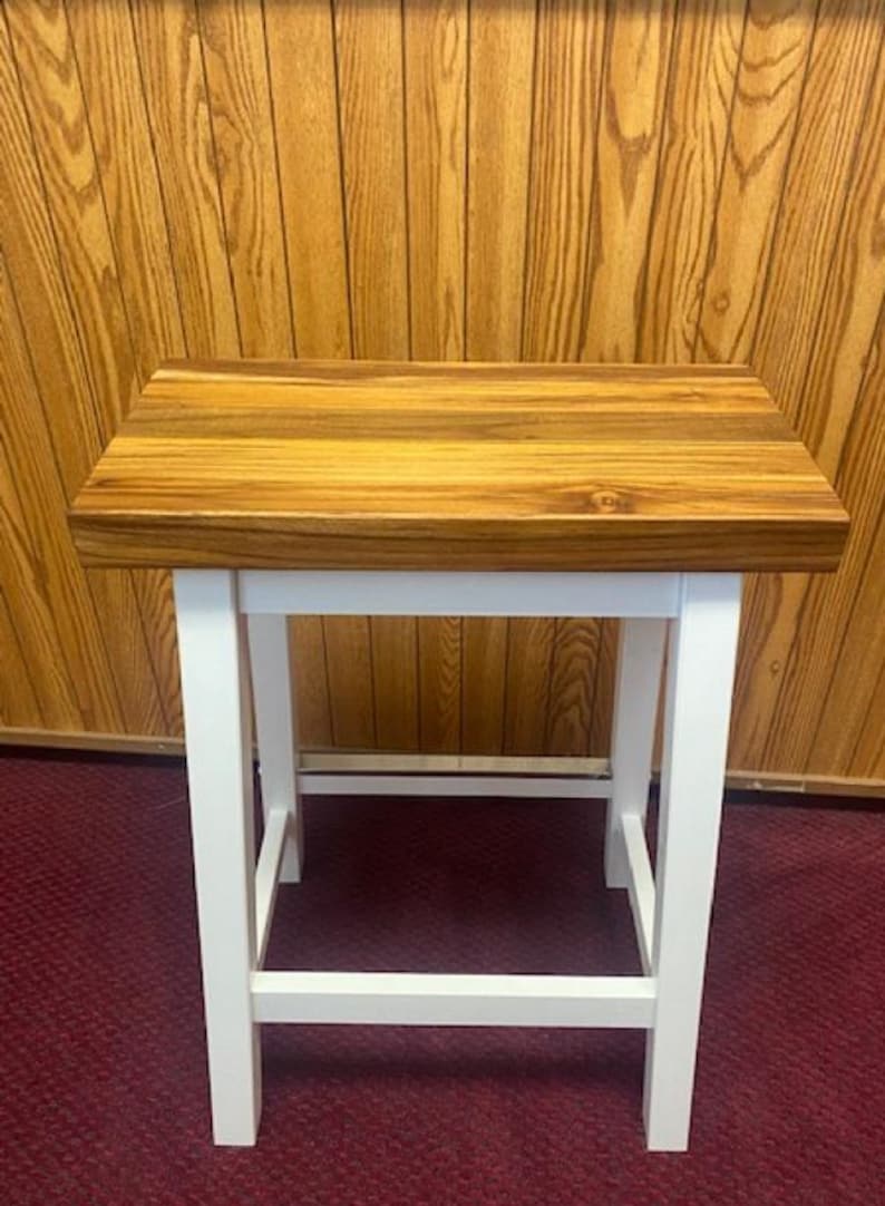 Peut inclure: Un tabouret en bois blanc avec un plateau en bois de boucher. Le plateau est en bois avec une finition naturelle. Le tabouret a un design simple avec quatre pieds et une barre transversale.