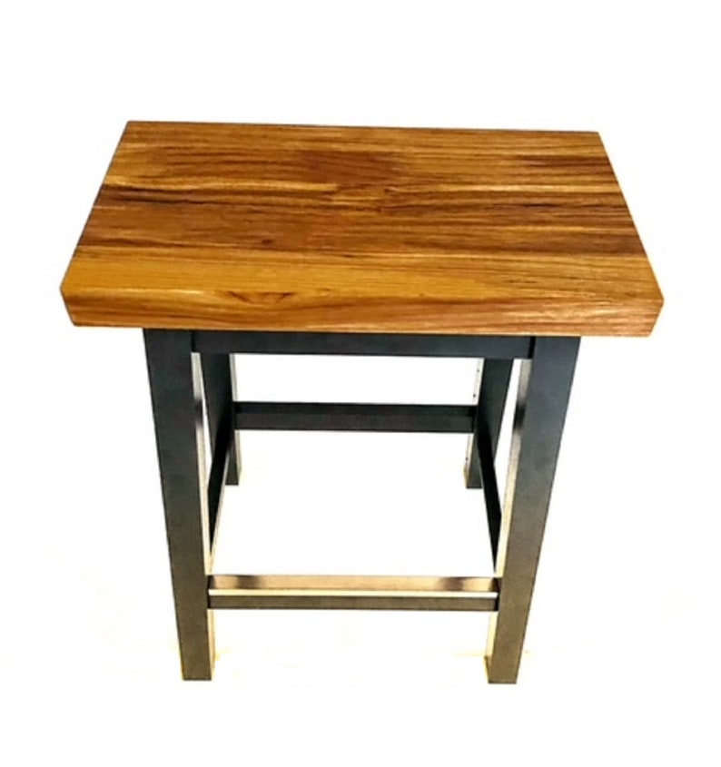 Peut inclure: Un tabouret en bois avec un plateau en bois naturel et des pieds en m&eacute;tal noir. Le tabouret a un design simple avec un plateau rectangulaire et une base carr&eacute;e.