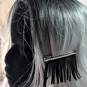 May include: A black hair clip with a row of rhinestones and a fringe of black tassels. The clip is in a silver tone.