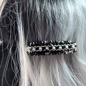 May include: Black and white hair clip with a tweed-like texture and gold accents.