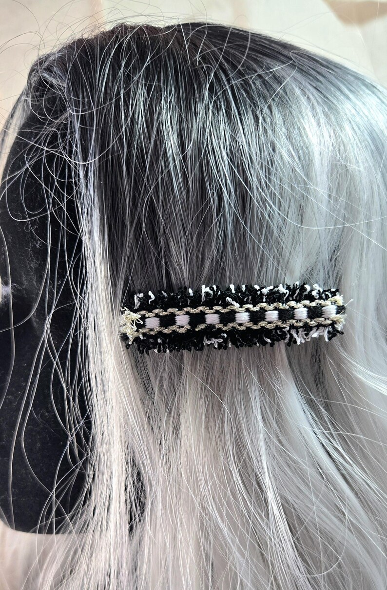 May include: Black and white hair clip with a tweed-like texture and gold accents.