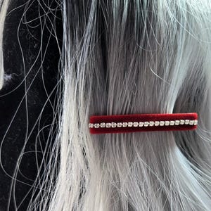 May include: A red velvet hair clip with a row of clear rhinestones.
