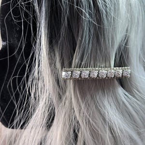 May include: A silver hair clip with a row of clear rhinestones. The clip is in the shape of a rectangle and has a textured surface.