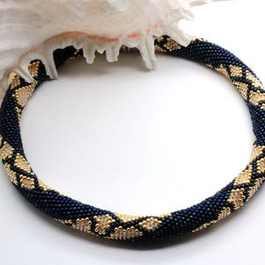 Op de afbeelding: Een donkerblauwe kralenketting met gouden accenten in een geometrisch patroon.