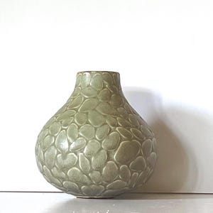May include: A sage green ceramic vase with a rounded, bulbous body and a narrow neck. The exterior surface features a raised, repeating pattern of smooth, pebble-like shapes that cover the entire body, creating a textured, tactile appearance.