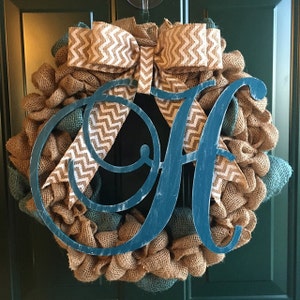 Puede incluir: Una corona de arpillera hecha a mano con una inicial de madera pintada de color turquesa. La corona presenta una mezcla de arpillera natural y turquesa, acentuada con un lazo de cinta con estampado de chevron. Decoración.