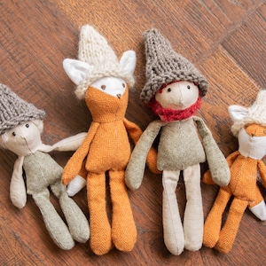Puede incluir: Cuatro juguetes de peluche hechos a mano con forma de zorros que llevan gorros de punto. Los zorros son naranja, gris y blanco con ojos marrones. Los gorros son grises, blancos y marrones.