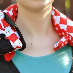 May include: A red and white checkered fabric dog toy with black felt ears and a black felt nose. The toy is worn around a person's neck as a scarf.