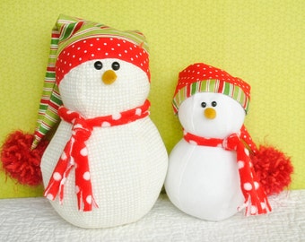 May include: Two white snowman ornaments with red and green striped hats and red scarves with white polka dots. The larger snowman has a red pom-pom on its hat.