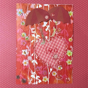 May include: A handmade greeting card with a red and pink floral design. Two maroon umbrellas are above a pink gingham heart that says "I You". The card is decorated with small flowers and white vines.