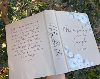 Puede incluir: Una Biblia beige con un diseño floral pintado a mano en blanco y verde salvia. La portada muestra los nombres McKinley y Joseph, la fecha 3.7.2026, y el lomo dice Holy Bible. La contraportada muestra el texto de Juan 15:9-12.