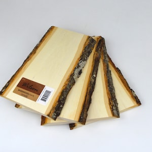 Puede incluir: Cuatro tablas de tilo con bordes de corteza natural. Las tablas son de color beige claro con rayas de vetas de madera más oscuras. Una etiqueta en una tabla dice "Wilson Basswood Plank (small)".
