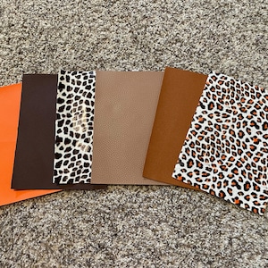 May include: A collection of leather and faux leather sheets in various colors and patterns. The sheets include solid orange, dark brown, tan, and brown, as well as sheets with leopard print patterns in black, white, and orange.