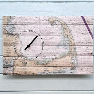 May include: A rectangular wooden clock with a nautical chart design. The clock face features a map with a tide indicator, labeled "High Tide," "Rising," "Low Tide," and "Falling." The clock hands are black.