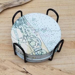 May include: Set of six round coasters featuring a nautical map of Ponce de Leon Inlet, Florida. The coasters are in a black metal holder.