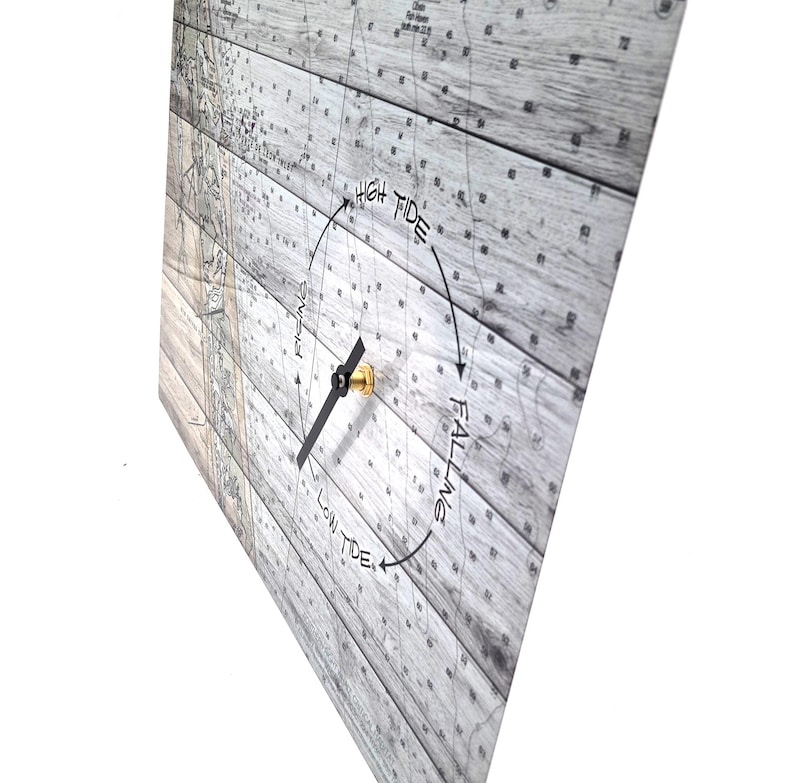 May include: A square tide clock featuring a nautical map background printed on a light gray wood grain pattern. The clock face displays the text High Tide, Low Tide, Rising, and Falling with a single black hand and a gold center mechanism.