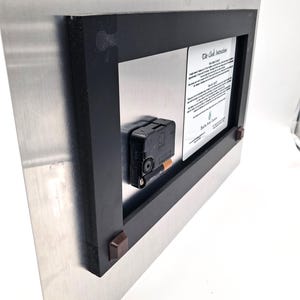 May include: The back of a rectangular metal clock featuring a black plastic frame, a central battery-operated clock mechanism with a single AA battery inserted, and a white instructional label titled The Tide Clock Instructions.