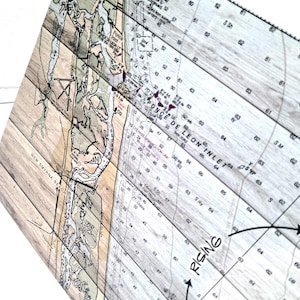 May include: A rectangular wooden wall art piece featuring a nautical chart of Ponce de Leon Inlet and New Smyrna Beach. The map is printed over light-toned wood planks with visible grain, displaying depth soundings, text, and geographic details.