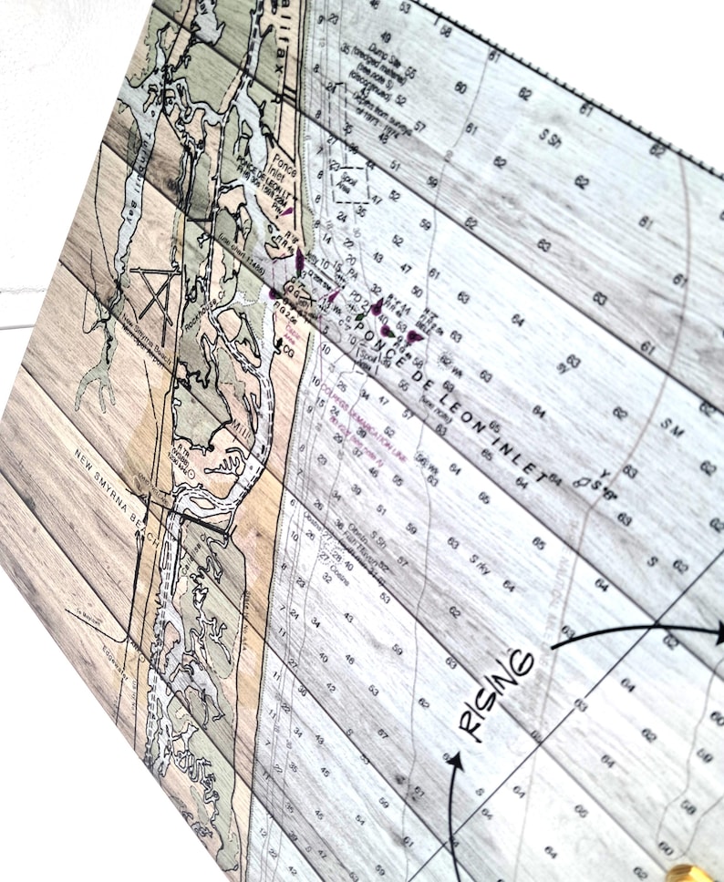 May include: A rectangular wooden wall art piece featuring a nautical chart of Ponce de Leon Inlet and New Smyrna Beach. The map is printed over light-toned wood planks with visible grain, displaying depth soundings, text, and geographic details.