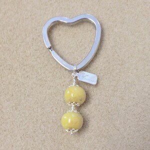 May include: A silver heart-shaped keyring with two yellow beads attached. The keyring has a small tag with the word "Handmade" on it.