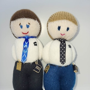 May include: Two knitted dolls dressed in white shirts with ties and blue pants. Both dolls have a small gold charm attached to their shirts that says "Holy Bible".
