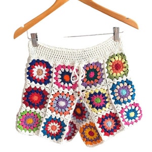 Op de afbeelding: Witte gehaakte shorts met een kleurrijk granny square patroon. De shorts hebben een trekkoord in de taille en een gegolfde zoom.