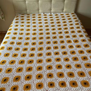 Puede incluir: Manta de crochet blanca con un patr&oacute;n repetitivo de girasoles amarillos y marrones.