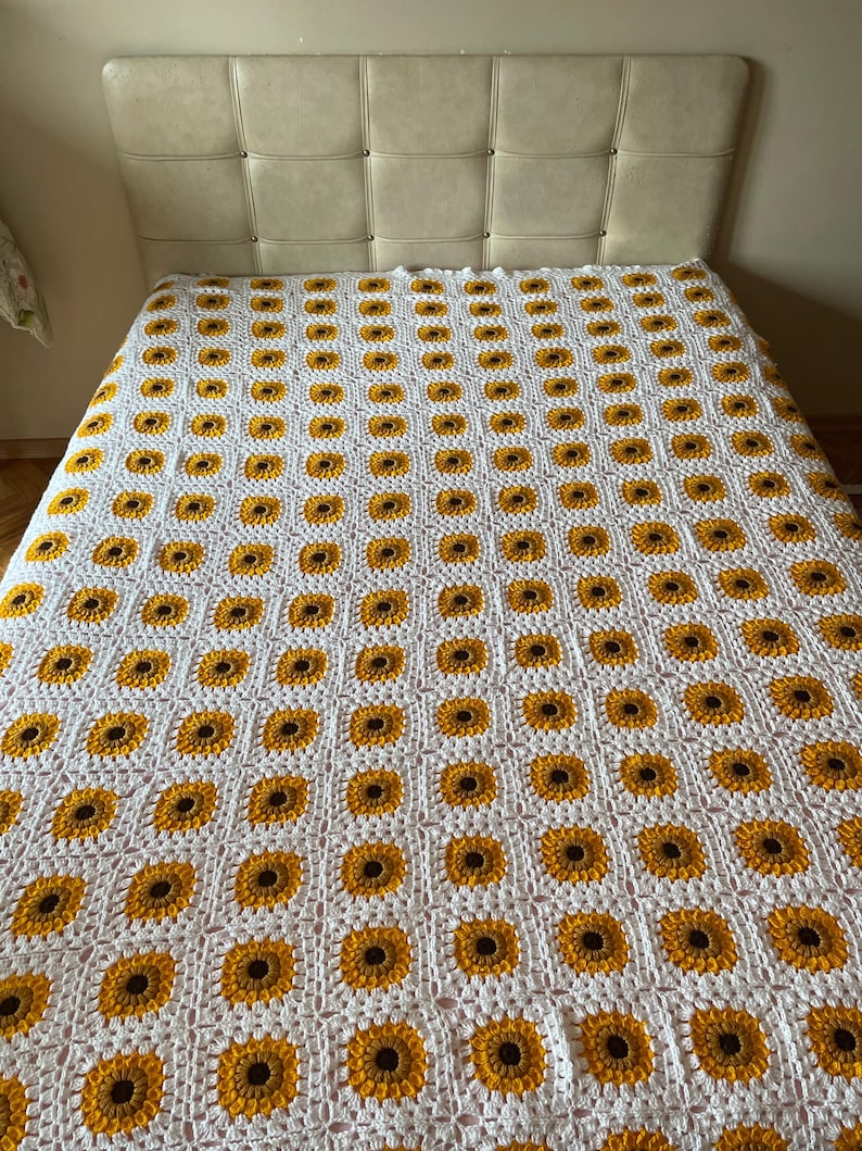 Puede incluir: Manta de crochet blanca con un patr&oacute;n repetitivo de girasoles amarillos y marrones.