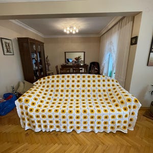 Puede incluir: Una manta de crochet blanca con un patr&oacute;n de girasol. La manta est&aacute; colocada sobre un sof&aacute; en una sala de estar.