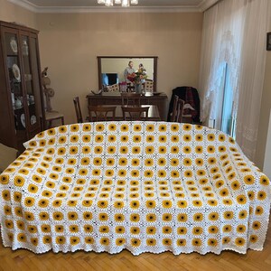 Puede incluir: Manta de crochet blanca con un patr&oacute;n de girasol. La manta est&aacute; en un sof&aacute; en una sala de estar.