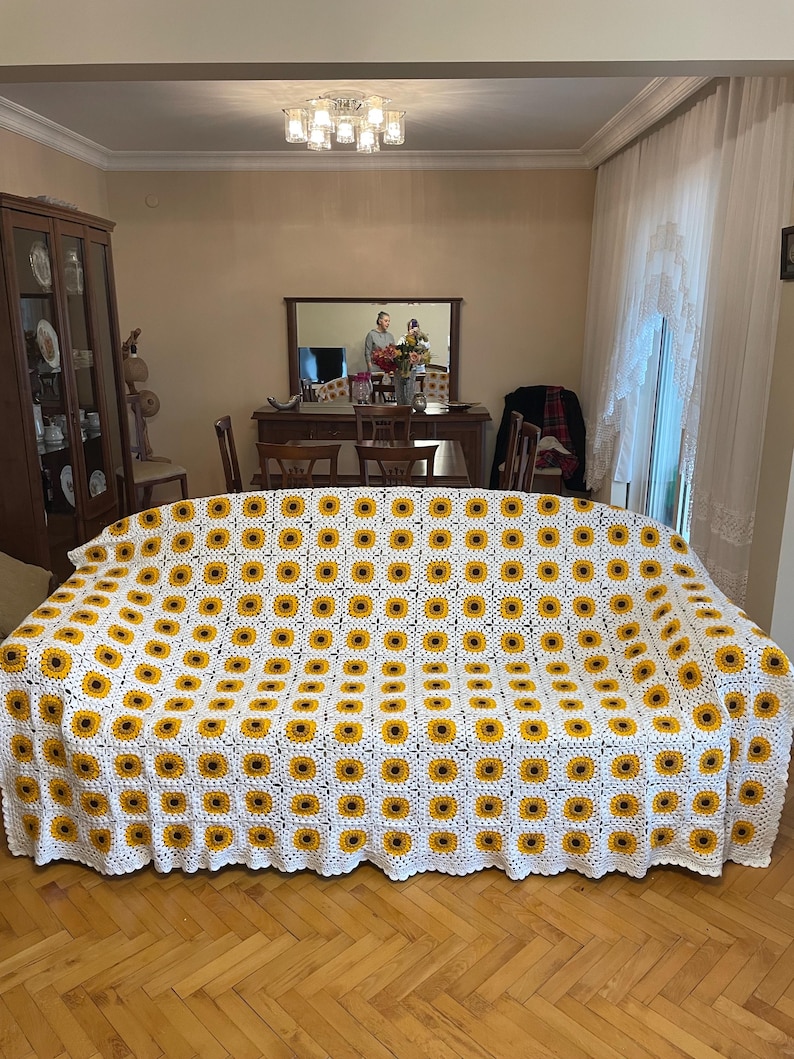 Puede incluir: Manta de crochet blanca con un patr&oacute;n de girasol. La manta est&aacute; en un sof&aacute; en una sala de estar.