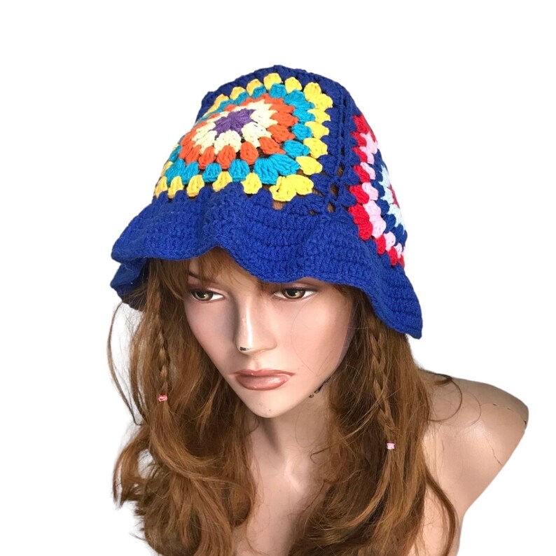 May include: A blue crochet bucket hat with a colorful square pattern on top. The square pattern features orange, yellow, blue, and purple. The hat has a scalloped brim. This handmade hat is a stylish accessory.