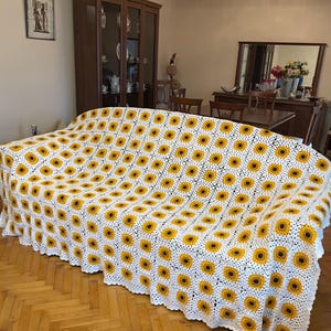 Puede incluir: Manta de crochet blanca con un patr&oacute;n de girasol. La manta est&aacute; colocada sobre un sof&aacute;.