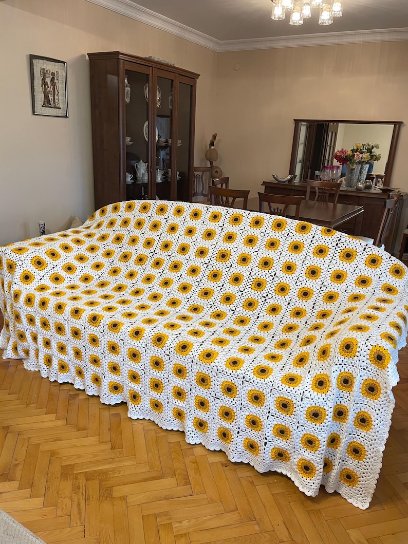 Puede incluir: Manta de crochet blanca con un patr&oacute;n de girasol. La manta est&aacute; colocada sobre un sof&aacute;.