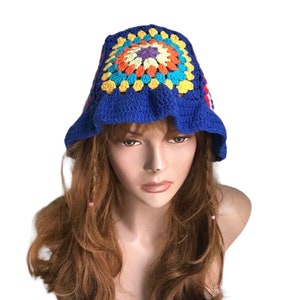 May include: A blue crochet bucket hat with a colorful floral design on top. The hat features a ruffled brim and is made of a soft, textured yarn. The floral design includes orange, yellow, and purple accents.