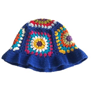 May include: A handmade, blue crochet bucket hat with a colorful, square pattern design. The squares feature a variety of colors, including yellow, pink, orange, and white. The hat has a ruffled brim.
