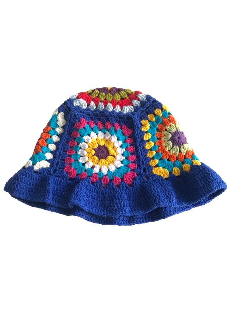May include: A handmade, blue crochet bucket hat with a colorful, square pattern design. The squares feature a variety of colors, including yellow, pink, orange, and white. The hat has a ruffled brim.